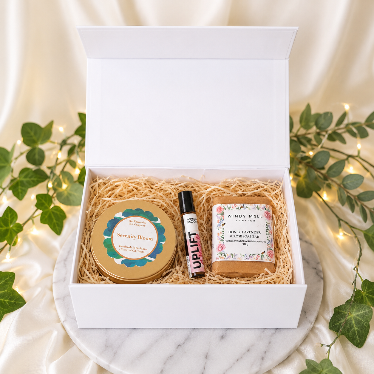 Gift set with products including a candle, diffuser, and soap in a decorative box on a marble surface.